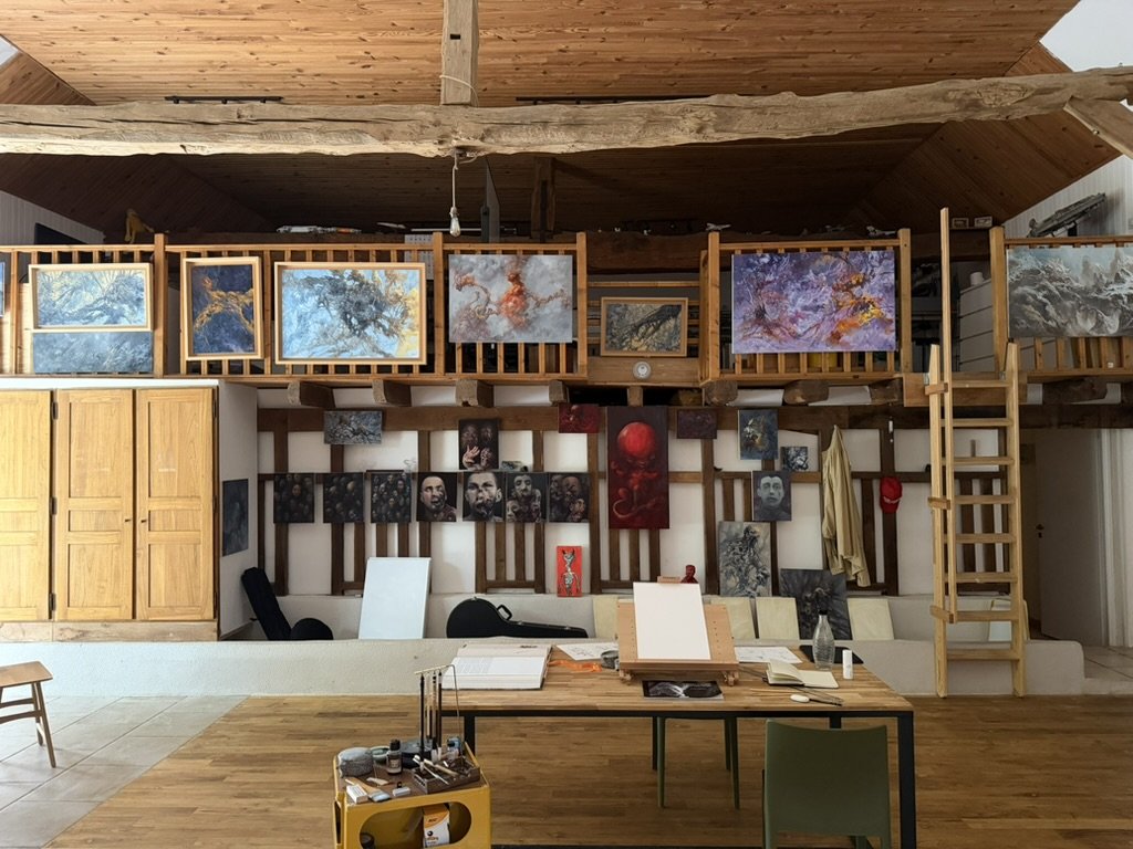 L'atelier sous charpente : les frondaisons alignées sur la mezzanine, les visages accrochés au mur du bas.